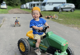 Et lille barn kører på en grøn legetøjstraktor på en vej i Camp Kyllburg, omgivet af campingvogne.