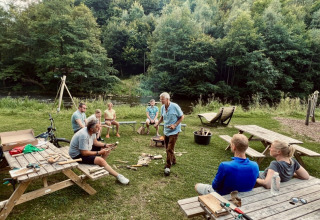 Gruppe mennesker sidder og står omkring borde i naturen ved Camp Kyllburg i Rheinland-Pfalz, Tyskland.