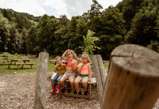 Tre børn sidder på en bænk i Camp Kyllburg-ferieparken i Tyskland og nyder is på en solrig dag.