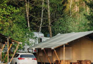 Una moderna tenda glamping e un’auto bianca in un parco vacanze verde tra gli alberi a Kyllburg, Germania.