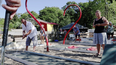 Folk spiller minigolf udendørs på Rosenvold Strand Camping i Danmark, omgivet af træer og afslappet stemning.
