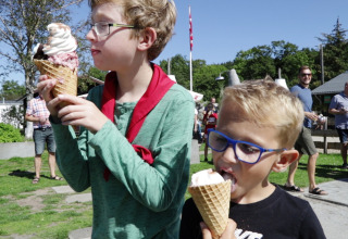 Twee jongens eten ijsjes bij Rosenvold Strand Camping in Denemarken, omringd door mensen op een zonnige dag.