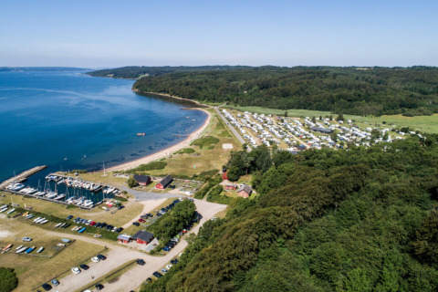 Luftfoto af Rosenvold Strand Camping i Danmark, med campingvogne, skov, strand og småbådehavn.