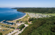 Luftfoto af Rosenvold Strand Camping i Danmark, med campingvogne, skov, strand og småbådehavn.
