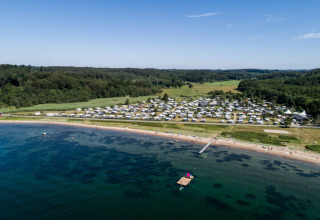 Luftfoto af Rosenvold Strand Camping med campingvogne, strand og skov i den centrale Danmark Region.