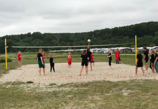 Folk spiller volleyball på sandbane ved Rosenvold Strand Camping, omgivet af grønt landskab i Danmark.