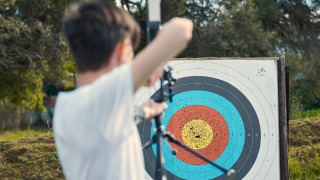 Enfant pratiquant le tir à l’arc sur un camping danois, vise une cible multicolore percée de flèches.