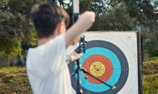 Niño practicando tiro con arco en un camping danés, apuntando con un arco a una diana de colores.