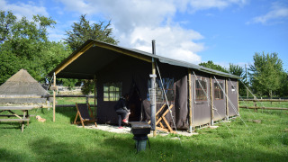 A safari tent in a grassy field, with a person near the entrance and a bright sky in the background.
