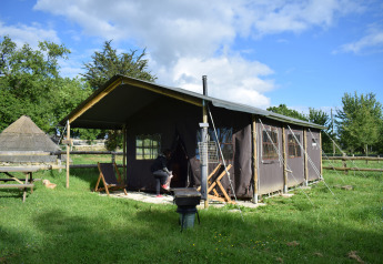 Safaritent in het gras met iemand aan de ingang en een mooie blauwe lucht erboven.