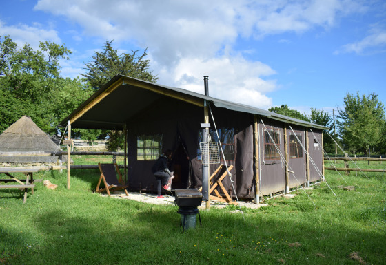 Tenda safari su un prato verde, una persona vicino all’ingresso e cielo azzurro sullo sfondo.