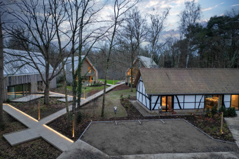 Chalets modernes en forêt au Woodz Lodges, parc de vacances en Limbourg belge, éclairés au crépuscule.