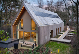 Moderne houten lodge met grote ramen en zonnepanelen in Woodz Lodges vakantiepark, Limburg, België.