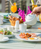 Escena de desayuno al aire libre en Woodz Lodges, Limburg, Bélgica, con jugo, café y comida fresca.