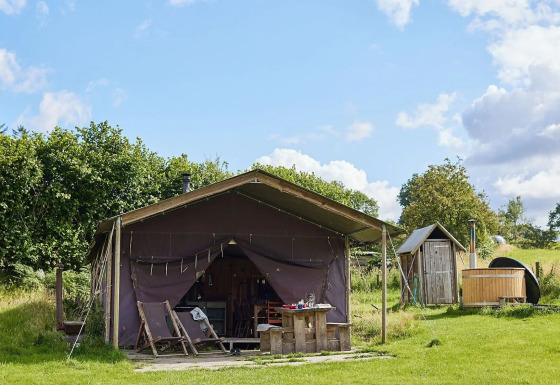 Safari tent at Feather Down Pant y March Farm, UK with private shower and outdoor hot tub on grassy field.