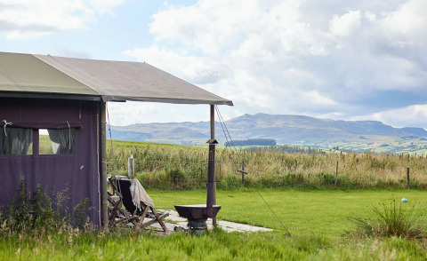 Safari-telt ved Feather Down Pant y March Farm i Storbritannien med udsigt over grønne marker og bakker.