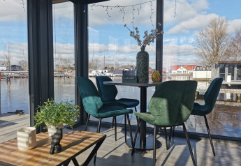 Innenansicht von Houseboat Heeg mit grünen Stühlen und Panoramablick auf den Jachthafen Heeg, Niederlande.