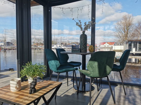Interieur van Houseboat Heeg met moderne groene stoelen, tafels en uitzicht op Marina Heeg, Nederland.
