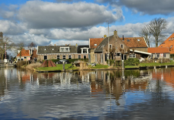 Husene og kanalen ved Houseboat Heeg i Marina Heeg, Holland, under en skyet og solrig himmel.