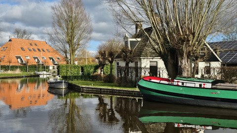 Foto einer Glamping-Unterkunft an einem Kanal mit Booten, Ziegelhaus und kahlen Bäumen im Winter.