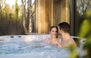 Stel in jacuzzi bij Lodge with Jacuzzi, proostend met champagne, genietend van de bosrijke omgeving.
