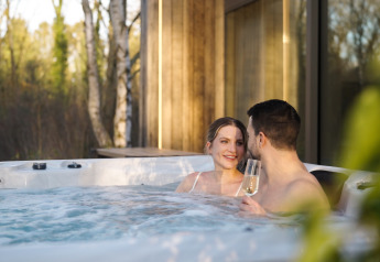 Koppel ontspant in een jacuzzi bij Lodge with Jacuzzi, klinkend met champagne, omringd door bomen.