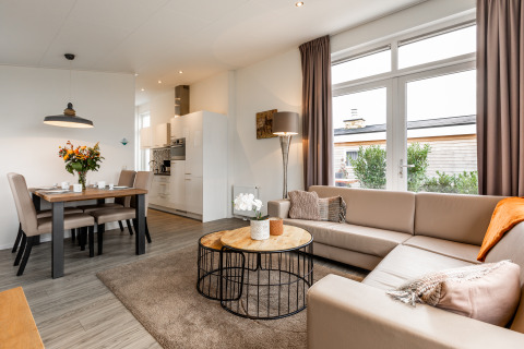 Lyst og moderne lodge-opholdsrum med hjørnesofa, spisebord, store vinduer og adgang til terrasse.
