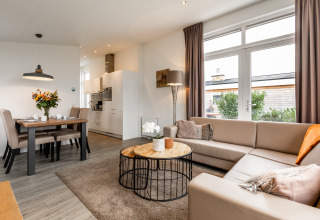 Lyst og moderne lodge-opholdsrum med hjørnesofa, spisebord, store vinduer og adgang til terrasse.