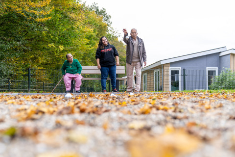 Drie mensen genieten buiten bij een glamping-accommodatie tussen herfstbladeren en moderne huisjes.