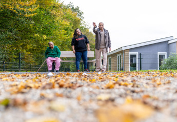 Tre personer hygger sig udendørs ved et glamping-sted, omgivet af efterårsblade og moderne bygninger.
