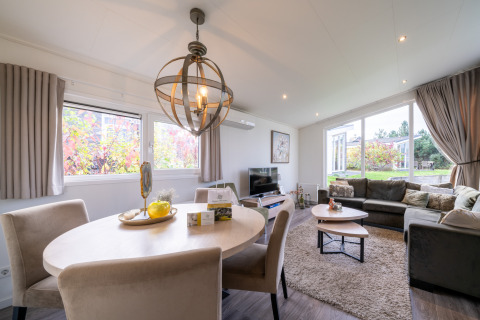 Lyst og moderne opholdsområde i en lodge med spisebord, sofahjørne og store vinduer med udsigt til have.