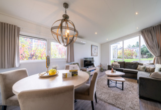 Lyst og moderne opholdsområde i en lodge med spisebord, sofahjørne og store vinduer med udsigt til have.