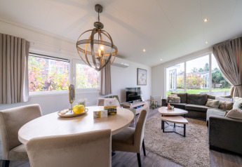 Lyst og moderne opholdsområde i en lodge med spisebord, sofahjørne og store vinduer med udsigt til have.