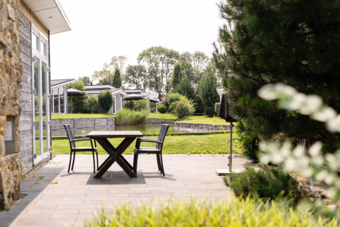 Terraza soleada junto a un lodge en Biebosch del Resort Mooi Bemelen, Países Bajos, con vista a jardín y agua.