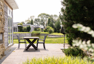 Terraza soleada junto a un lodge en Biebosch del Resort Mooi Bemelen, Países Bajos, con vista a jardín y agua.