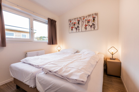 Acogedor dormitorio de lodge con cama doble, mesitas, lámparas modernas y ventana con cortinas.