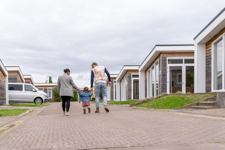 A family walks hand in hand with a small child along a paved path in a modern lodge complex.