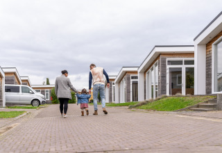 A family walks hand in hand with a small child along a paved path in a modern lodge complex.