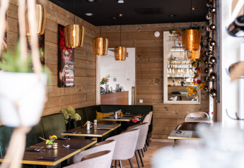 Moderne restaurantinteriør med træpaneler, grønne sofaer og gyldne lamper på Biebosch - Sunshower, Resort Mooi Bemelen.