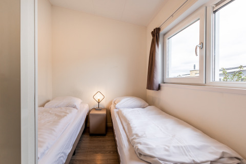 Et simpelt soveværelse i en lodge med to enkeltsenge, et lille natbord og et vindue med gardiner.