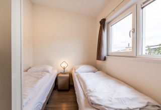 Habitación sencilla en una cabaña con dos camas individuales, una mesita y una ventana.