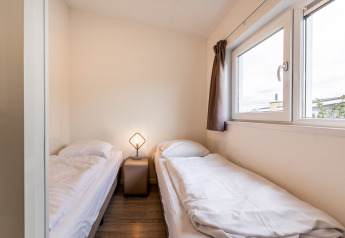 Et simpelt soveværelse i en lodge med to enkeltsenge, et lille natbord og et vindue med gardiner.