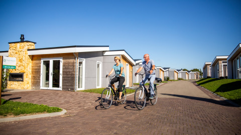 Dos personas andando en bicicleta frente a la Biebosch - Sunshower lodge en Resort Mooi Bemelen, Países Bajos.