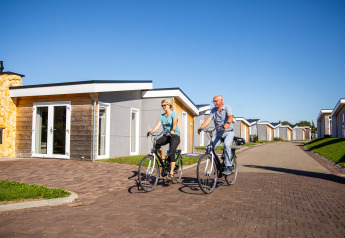 To personer cykler foran Biebosch - Sunshower-lodgen på Resort Mooi Bemelen i Holland på en solrig dag.