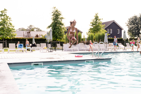 Een kind springt in het zwembad van Resort Mooi Bemelen, met ligstoelen en gasten aan de rand.