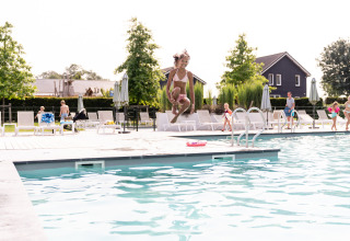 Un enfant saute dans une piscine au Resort Mooi Bemelen, entouré de transats et d’autres vacanciers.