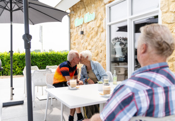 Ældre par kysser på caféen Ciao Ciao ved Resort Mooi Bemelen, mens en ven ser til i forgrunden.