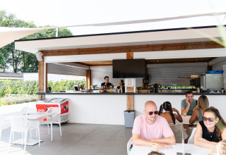 Bar y zona de comedor al aire libre en Biebosch - tuinhuis, Resort Mooi Bemelen, con huéspedes relajados.
