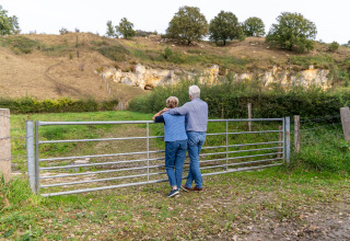 Pareja mayor contempla el paisaje junto a una verja metálica durante su estancia de glamping.