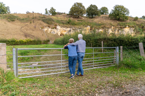 Ouder koppel bij een hek, genietend van het landschap aan hun glampingaccommodatie in de natuur.